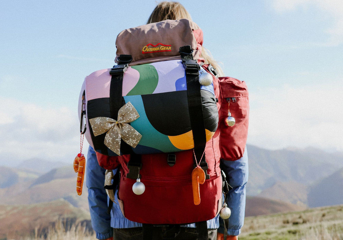 Hiker in the mountains with a colorful VOITED Cloudtouch blanket strapped to a festively decorated backpack.
