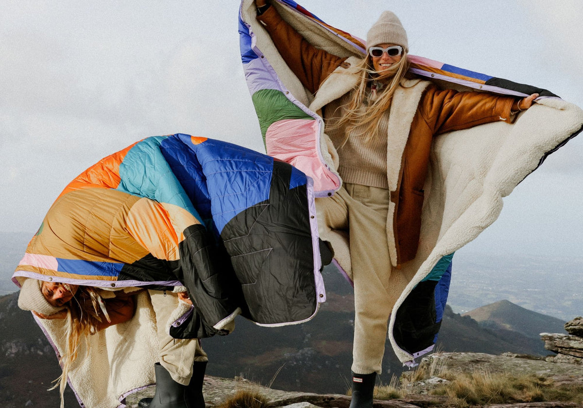 VOITED Cloudtouch Value Set bundle offer: two women on a mountaintop holding two Cloudtouch blankets with a colorful patchwork design and sherpa lining, fluttering in the wind.