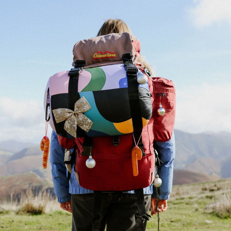 Hiker in the mountains with a colorful VOITED Cloudtouch blanket strapped to a festively decorated backpack.